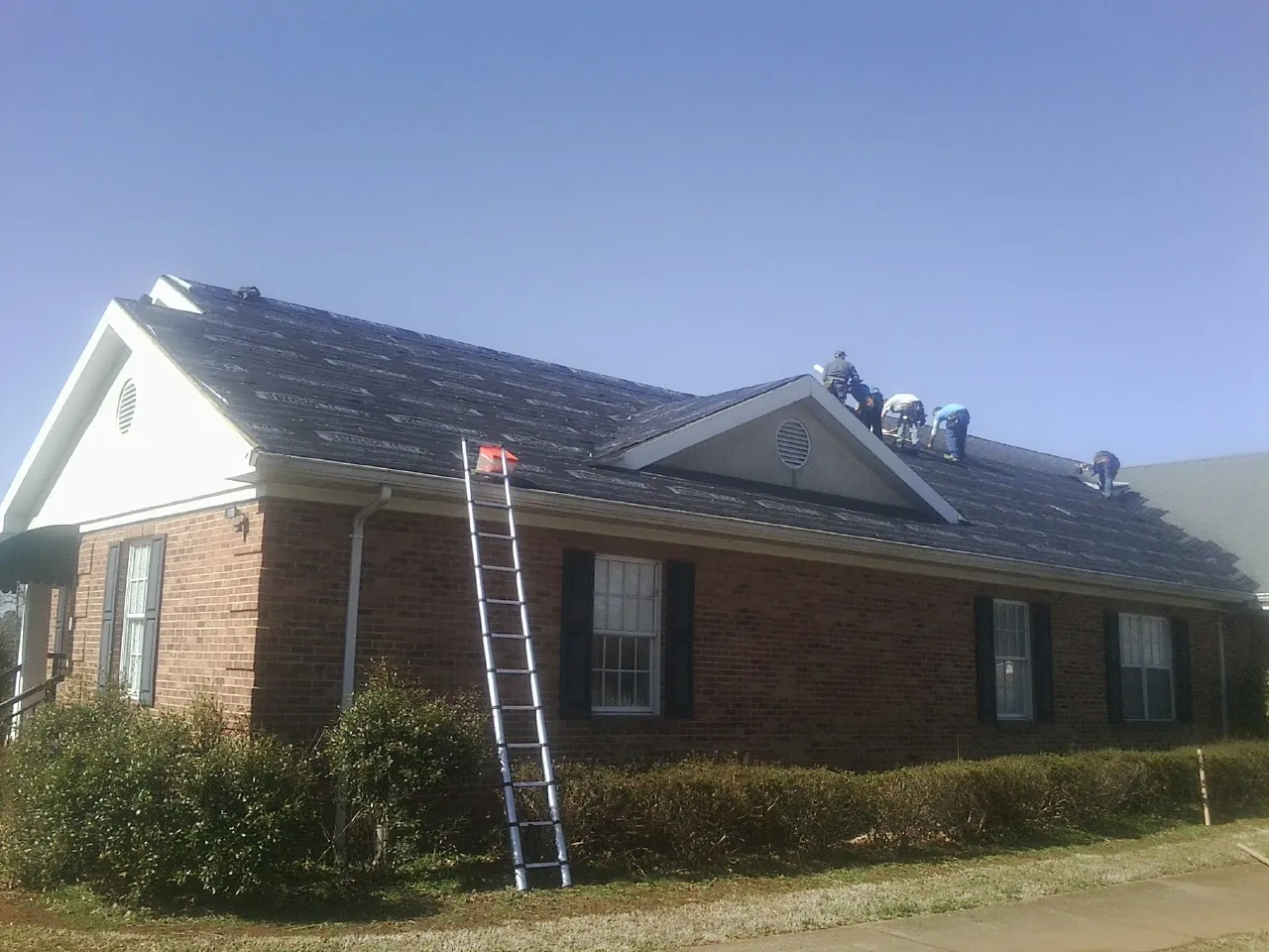 Crew tearing shingles off a brick ranch roof with a ladder set — Emergency Roof Repair work by our crew in Bird In Hand