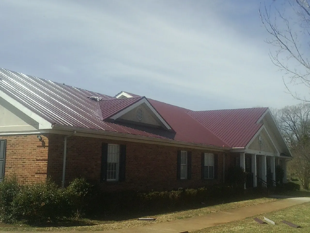 Red metal roof with gabled entries on a long brick building, from a Hail Damage Roof Repair job in Bird In Hand