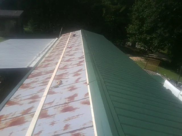 Old rusted panels beside newly installed green metal roofing — Wind Damage Roof Repair by Roofing Brothers in Bird In Hand