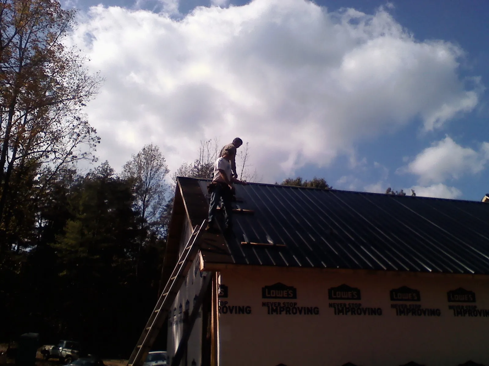 Roofer fastening dark metal panels high against a cloudy sky, from a Roof Inspection job in Bird In Hand