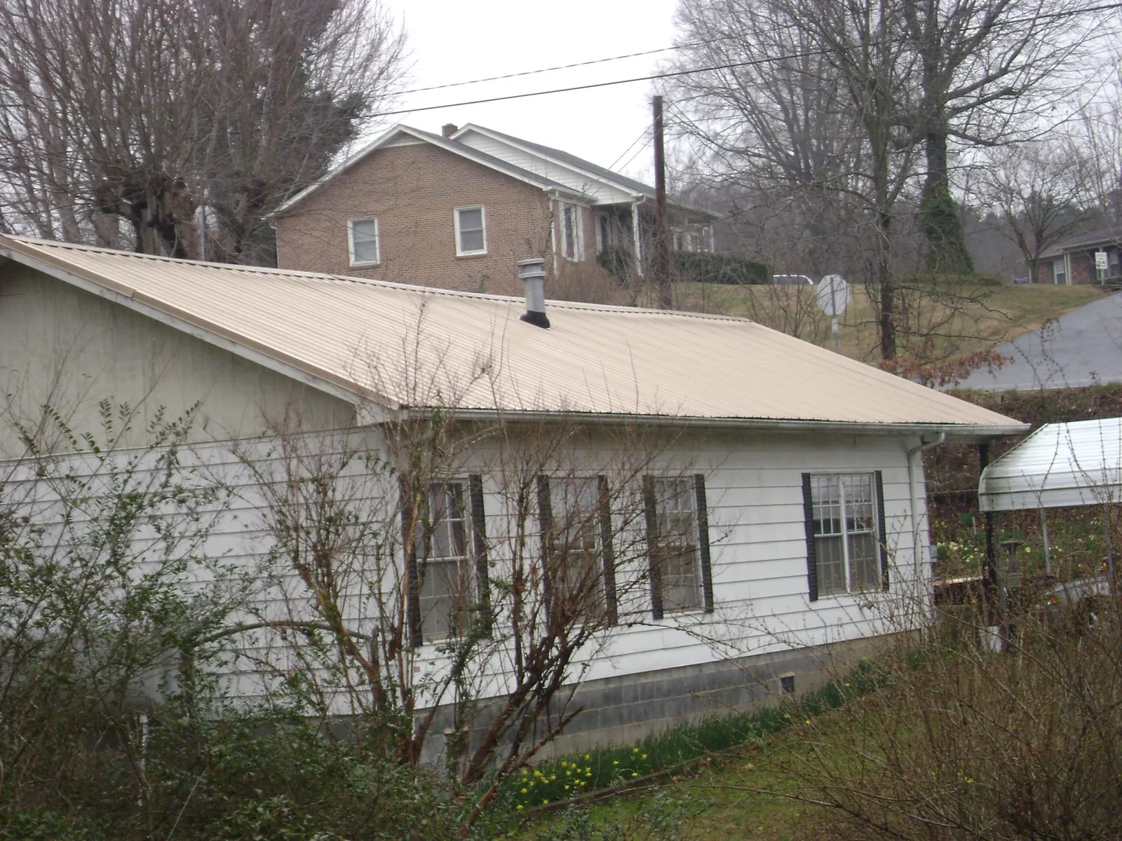 Tan metal roof on a white sided house set into a hillside — Commercial Roofing by Roofing Brothers in Bird In Hand
